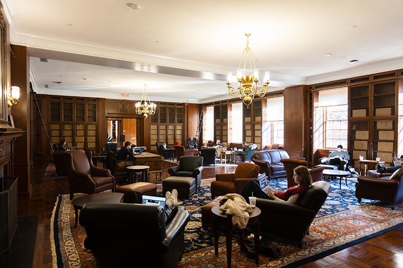 Students study in an ornate room in Alderman Library. The room has Persian rugs, leather chairs, dark wood bookshelves, and a fireplace.