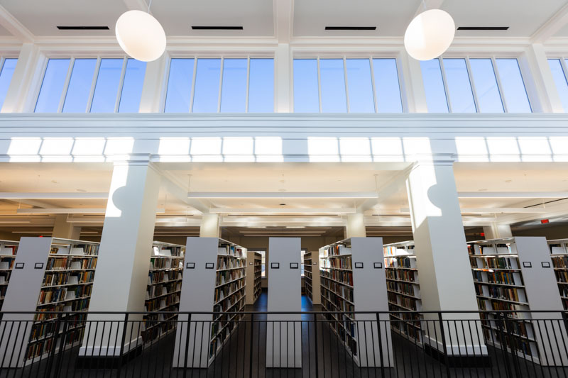 Sunlight shines through clerestory windows onto numerous shelves of books on the fifth floor.